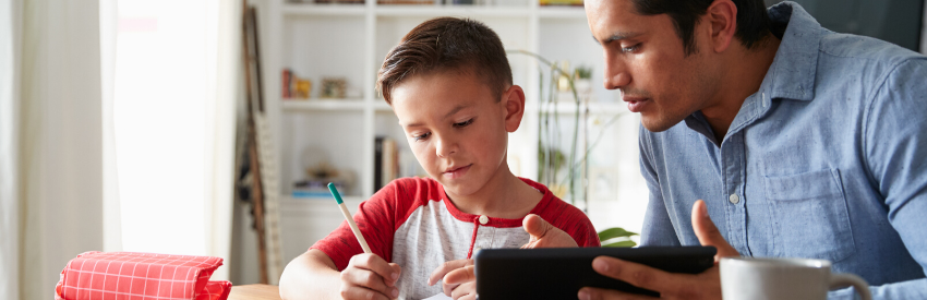 Adult and child working together at a table, looking at a tablet and mixing ingredients in a bright kitchen.