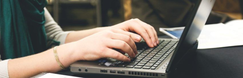 Hands typing on a laptop at a desk, with a notebook nearby.