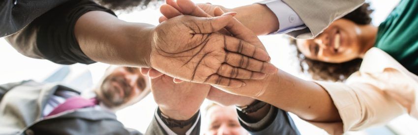 Hands stacked together in a teamwork gesture against a bright office background