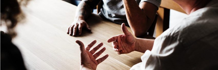 People in a meeting around a table, gesturing during a discussion