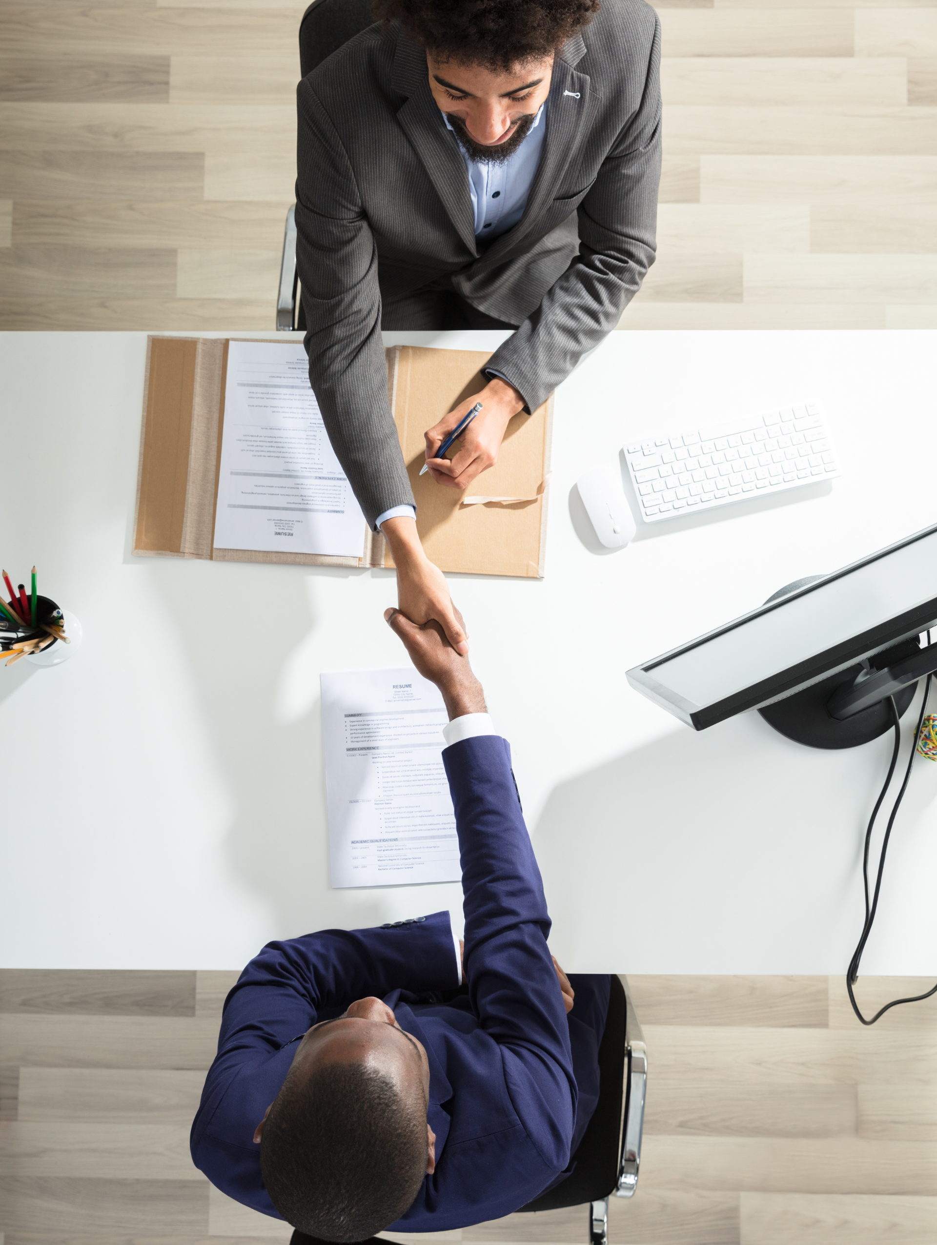 Two office workers shaking hands across a desk during a meeting
