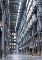 Tall warehouse aisle with stacked shelves of boxes and pallets under bright overhead lights
