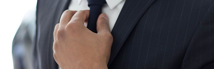Hand adjusting a black tie on a dark pinstripe suit