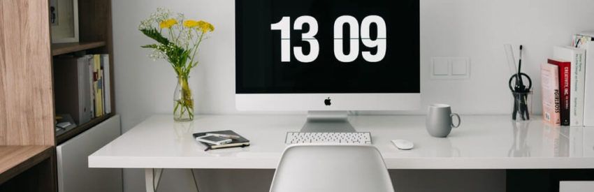 Minimal white desk setup with iMac, chair, flowers, and clock reading 13:09