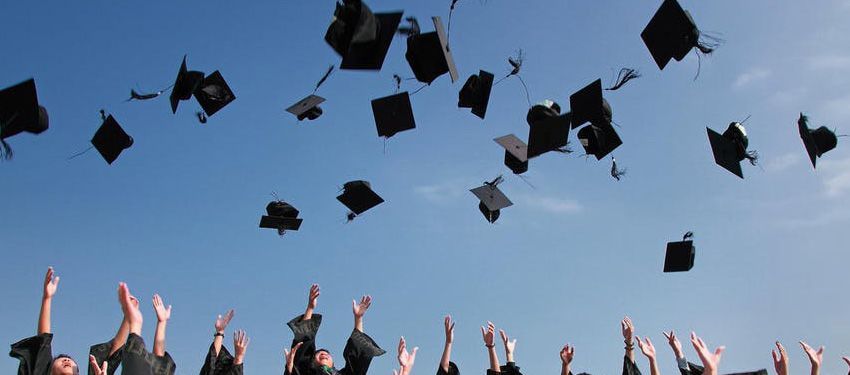 Graduates tossing black caps into a blue sky during a celebration