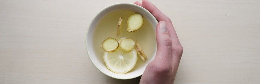 Hand holding a bowl of soup with sliced potatoes and onion on a light table