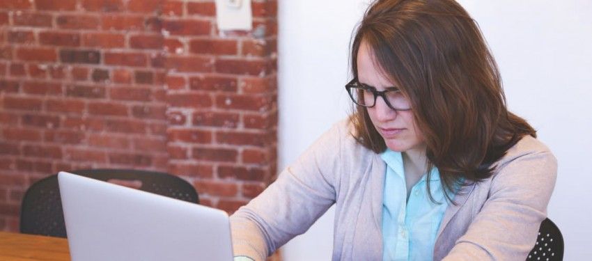 Person working on a laptop at a desk in front of a brick wall