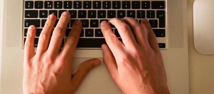 Hands typing on a laptop keyboard beside a white mouse on a desk.