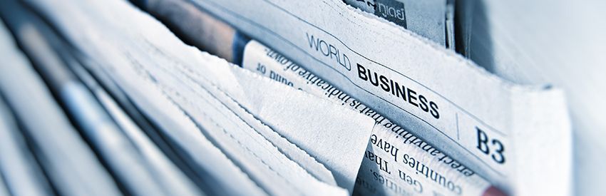 Stack of folded newspapers with a visible business section headline in blue tones.