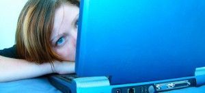 Woman peeking over a blue laptop, resting her head on her arm