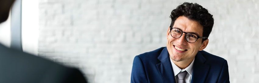 Smiling man in a navy suit and glasses in a bright office setting