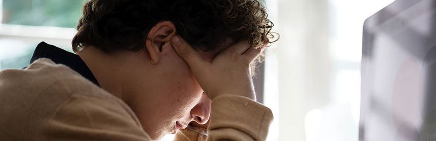 Person holding their head at a desk, looking stressed or tired near a computer screen.