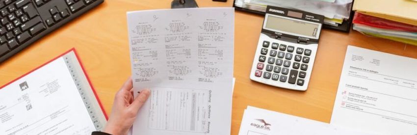 Hands holding paperwork on a desk with a calculator, keyboard, and scattered documents.