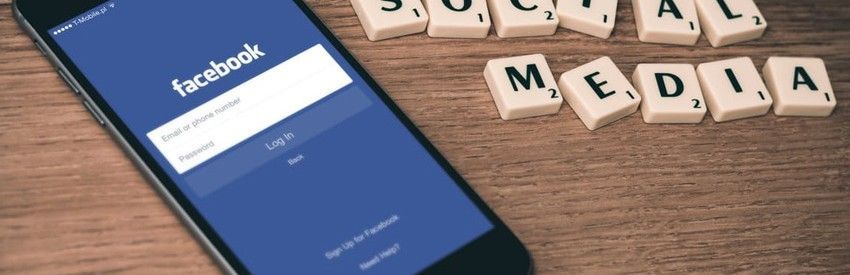 Facebook login screen on a smartphone beside wooden letter blocks spelling “social media”