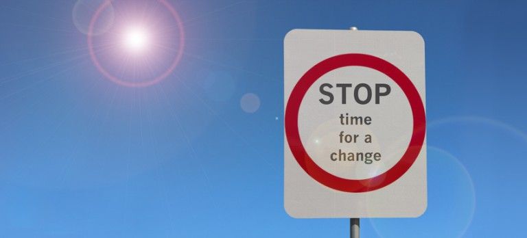 Road sign with red circle reading “STOP time for a change” against a blue sky.