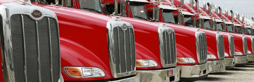Row of red semi-trucks parked in a line, showing their chrome grilles and front ends