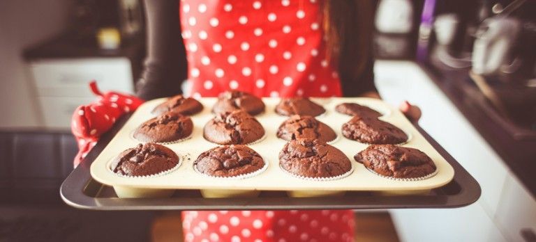 Tray of freshly baked chocolate pastries on parchment paper, held by a person in a red polka-dot apron