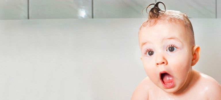 Surprised baby in a bathtub with wet hair and wide-open mouth