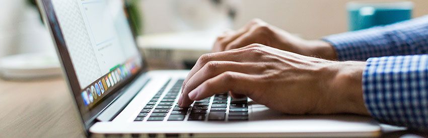 Hands typing on a laptop keyboard beside a colorful screen close-up