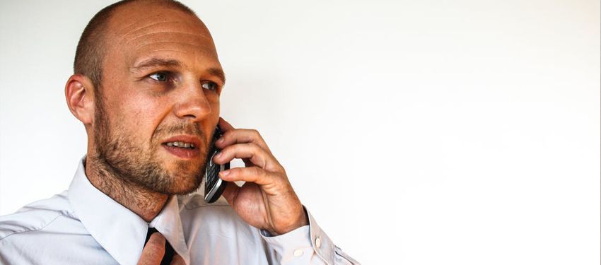 Man in white shirt talking on a cellphone, looking focused against a plain white background