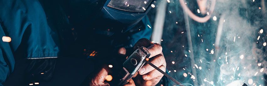 Welding sparks fly as gloved hands work on metal in a dark workshop