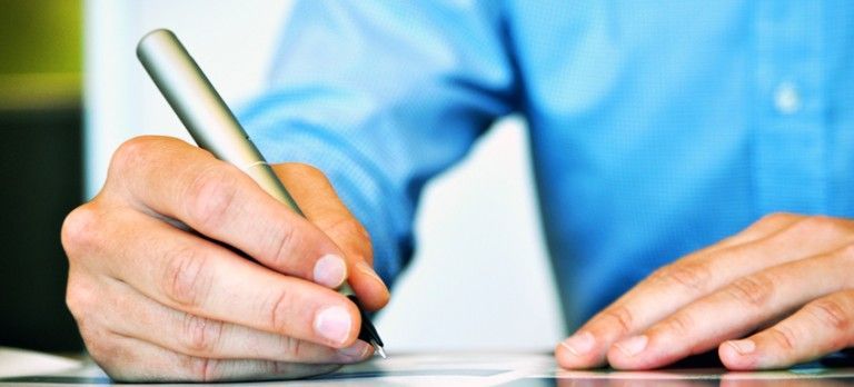 Hands using a pen to write on paper at a desk