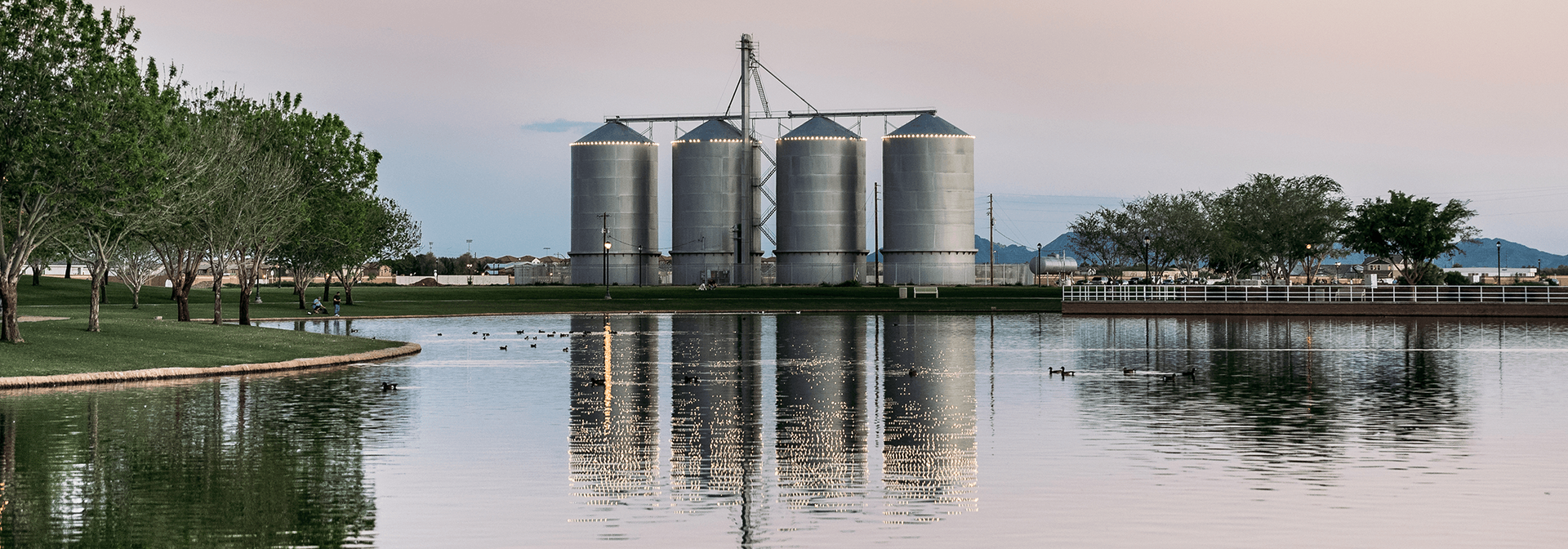 A row of silos are reflected in a body of water.