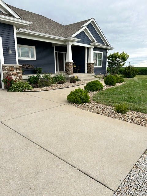 Modern suburban house with dark blue siding, stone accents, and a wide concrete driveway beside a lawn.