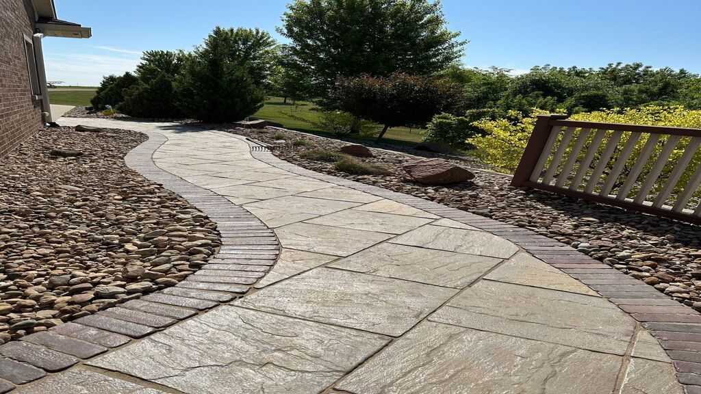 Curved stone walkway through a landscaped garden with rock borders and a wooden fence