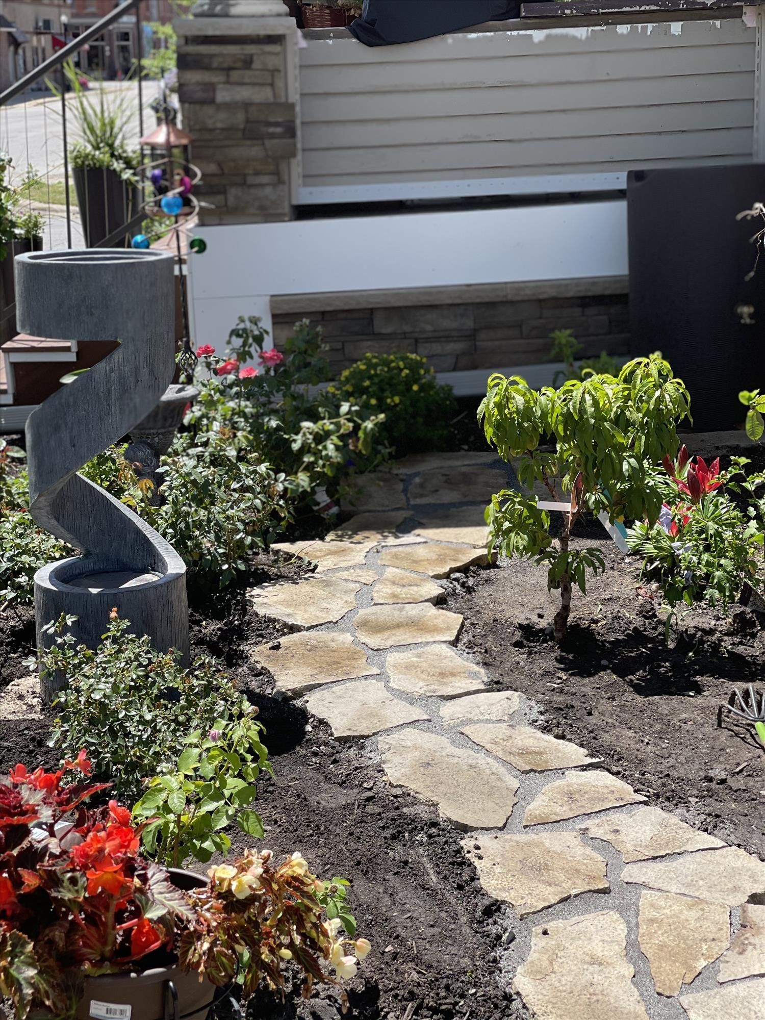 Stone garden path lined with flowers leading to a white garage gate and stone planter.
