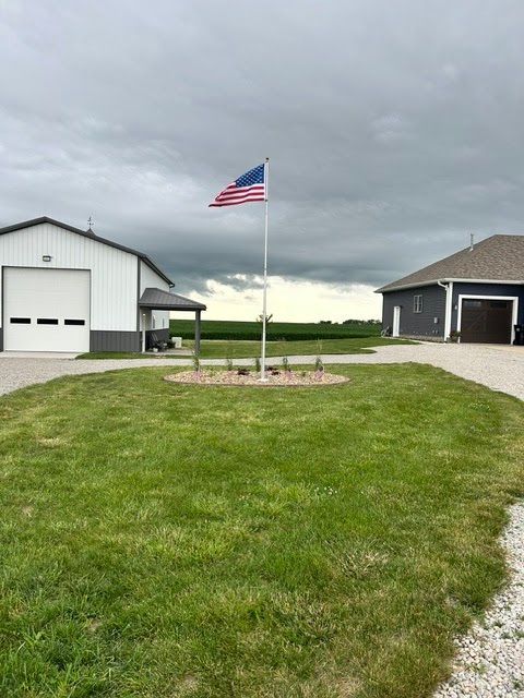 American flag on a flagpole between two buildings, with a grassy yard under a cloudy sky.