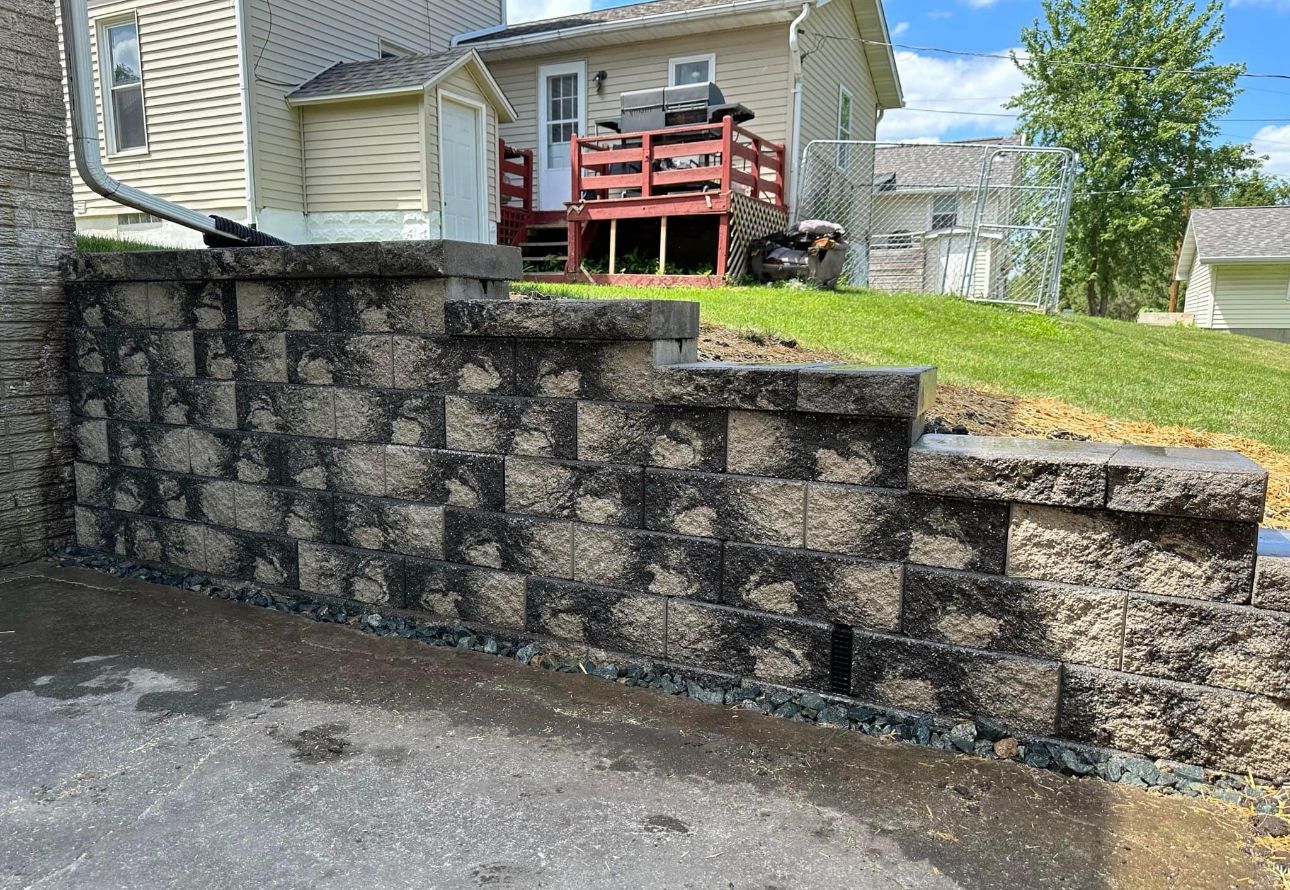 Stone retaining wall with steps in a residential yard beside a house and driveway