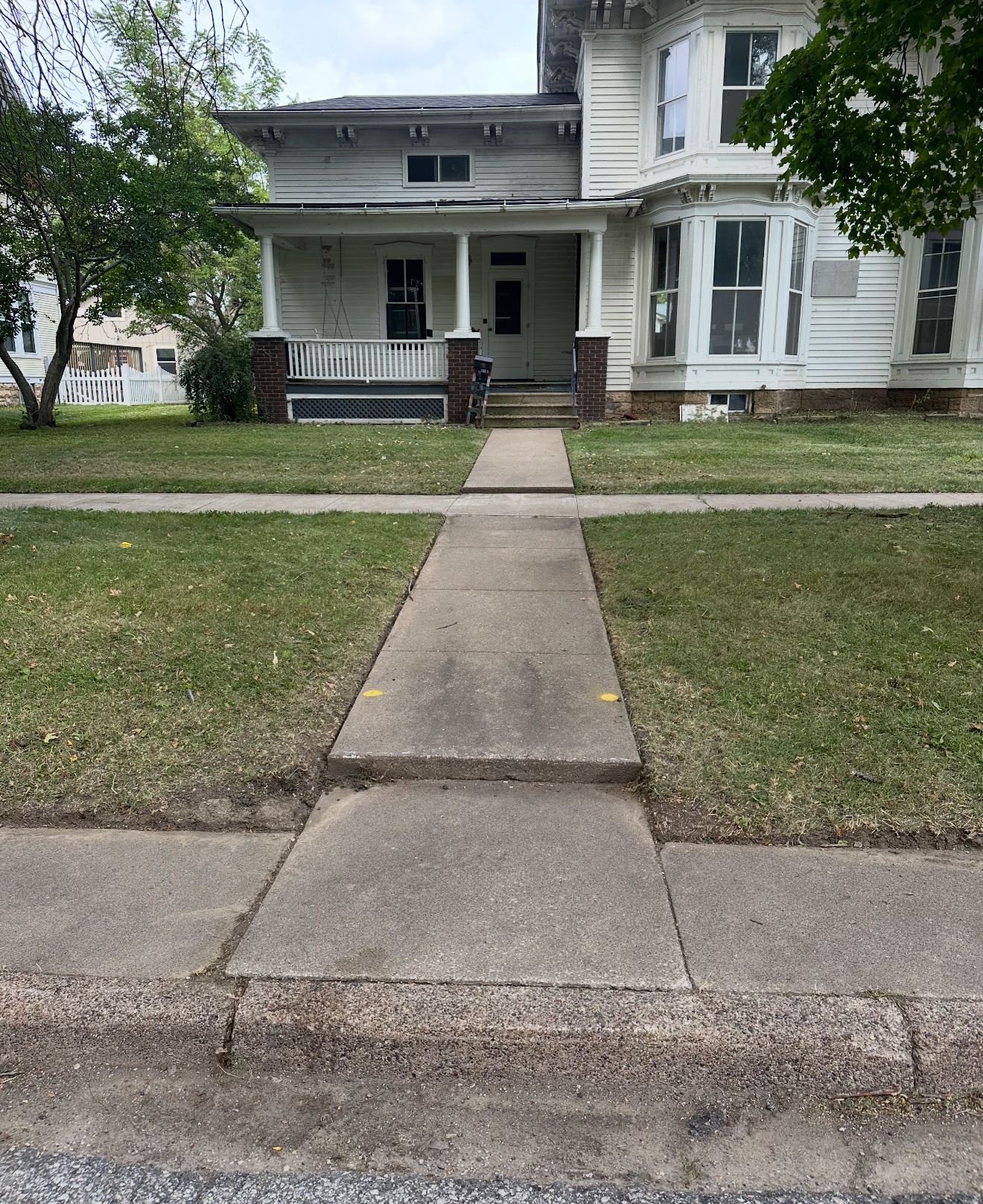 White two-story house with a front porch and a concrete walkway across a small lawn
