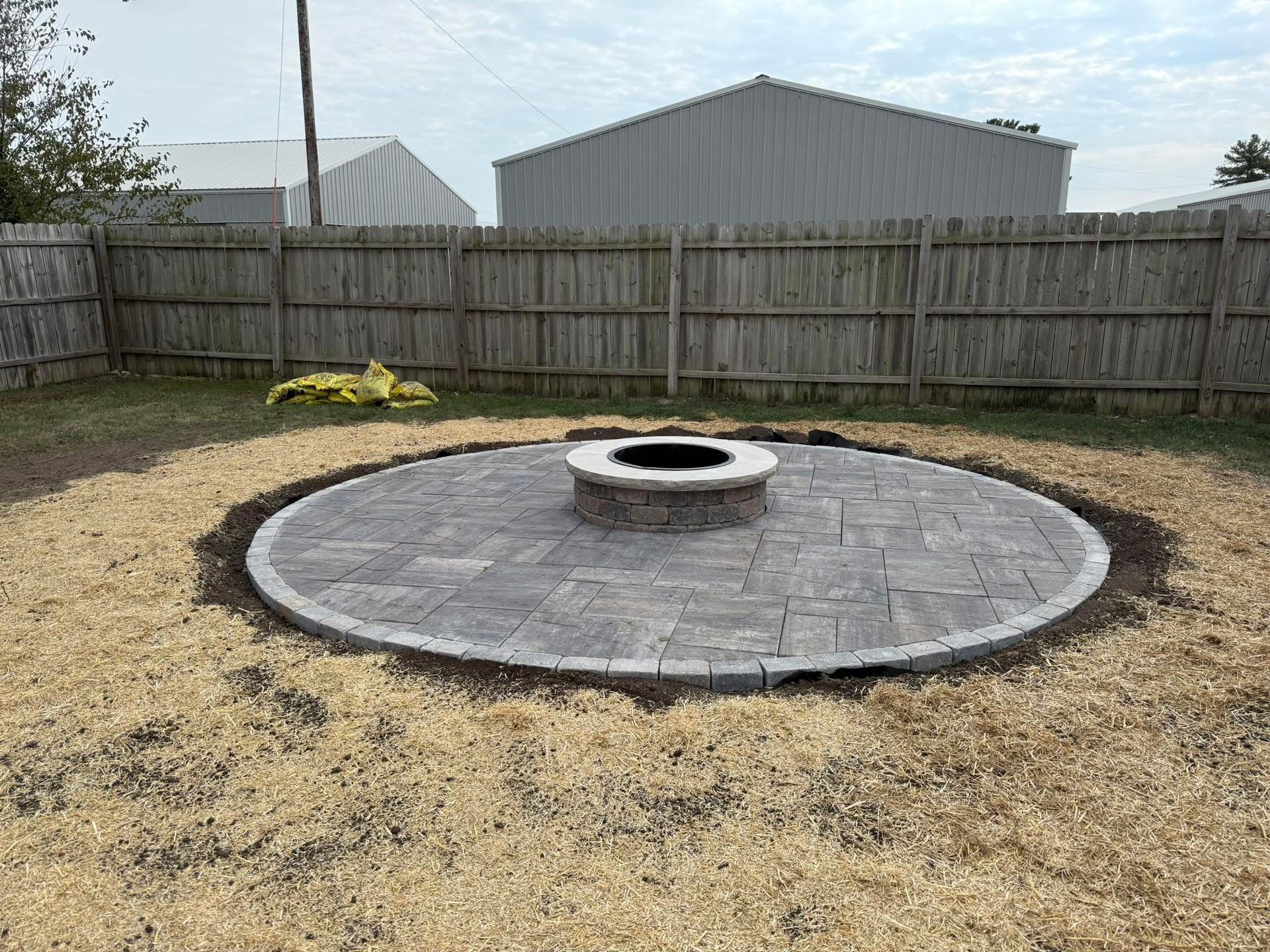 Circular stone fire pit in a fenced backyard with a small yellow chair nearby.