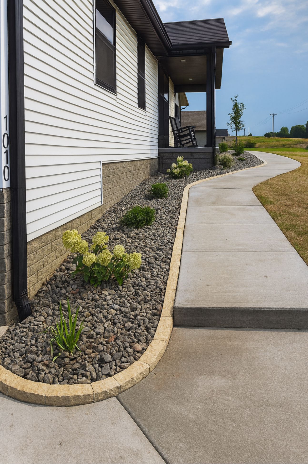 Sidewalk beside a white house with a rock garden and concrete curb ramp leading along the path