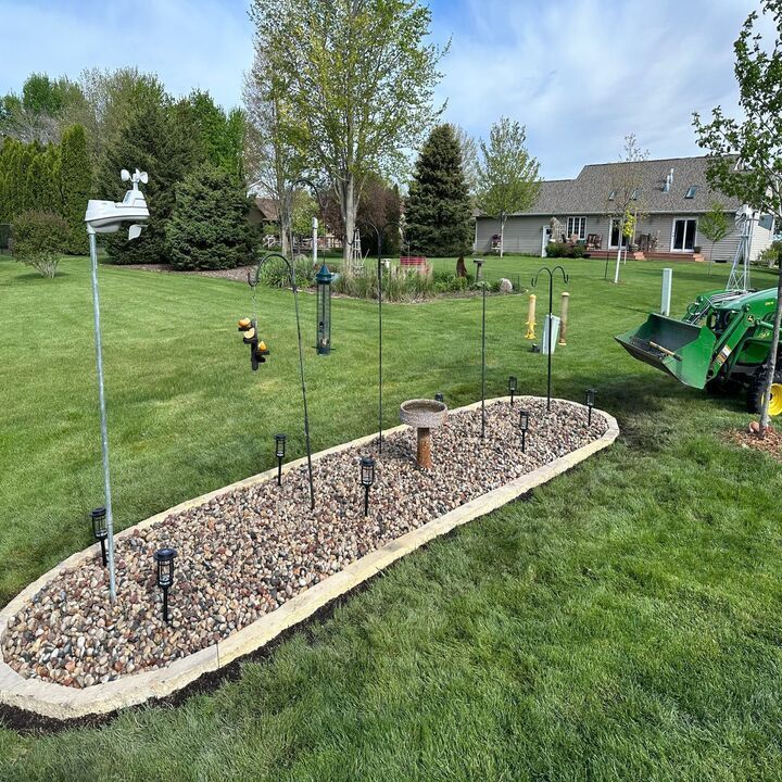 Backyard garden bed with gravel mulch, stepping stones, and small solar lights on a green lawn