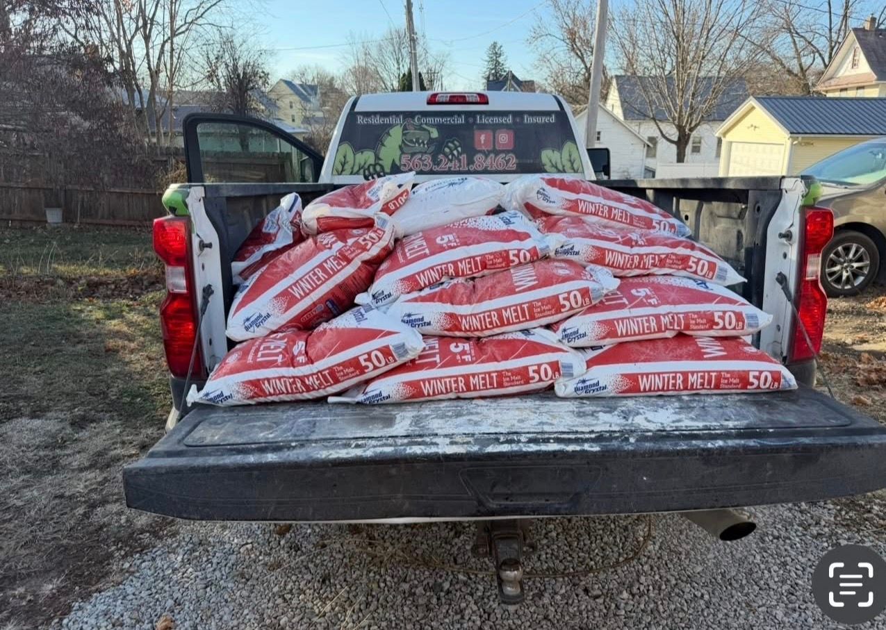 Pickup truck bed loaded with stacked red-and-white bags, tailgate down in a driveway.