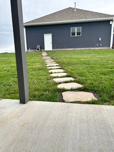 Concrete patio facing a grassy yard with stepping stones leading to a dark gray house