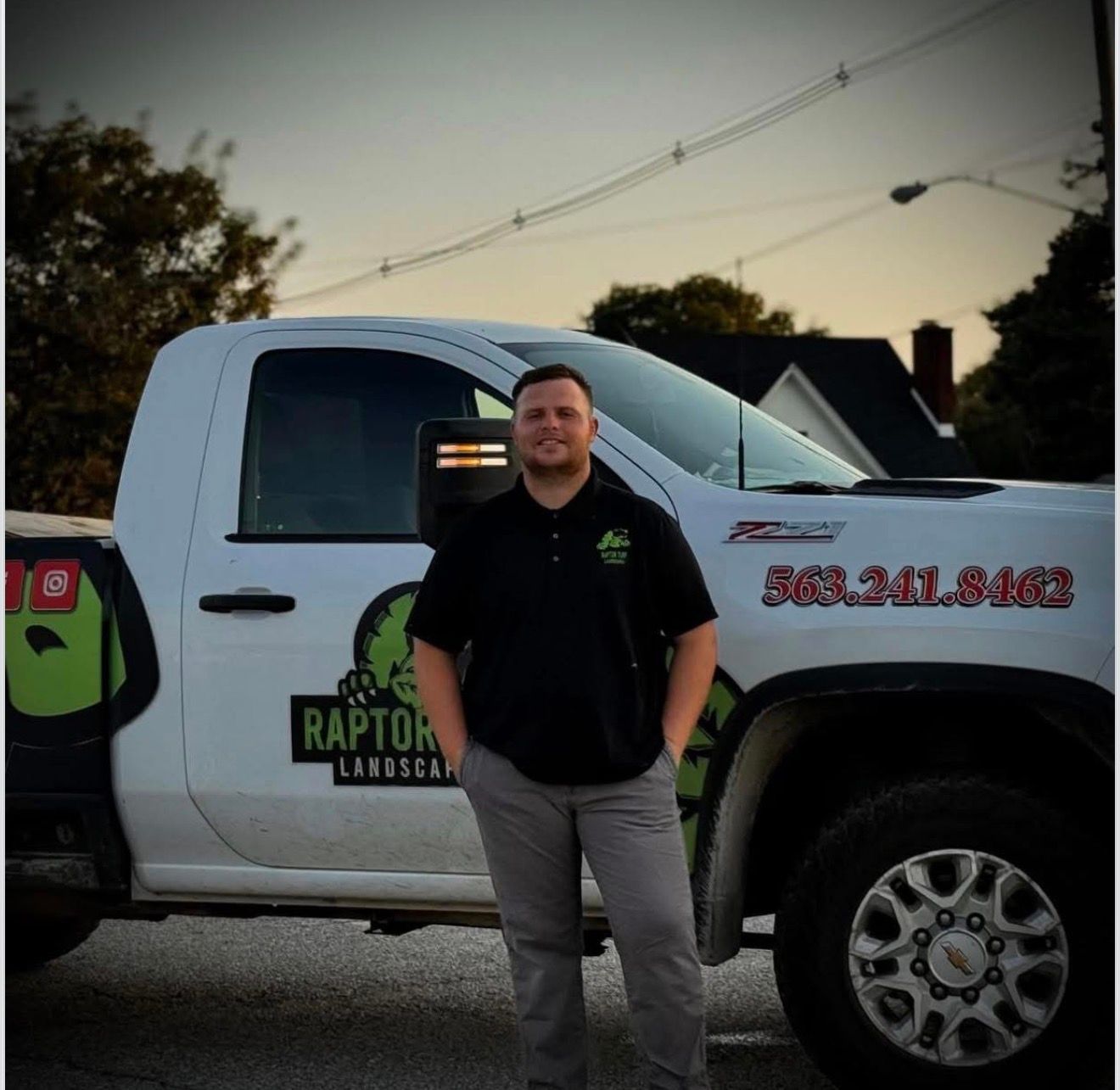 Man standing in front of a white Raptor Landscaping pickup truck at dusk