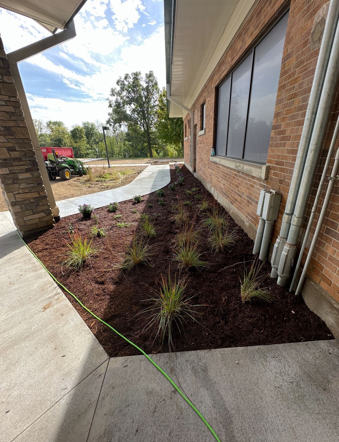 Landscaped mulch bed beside a brick building with windows and a concrete walkway