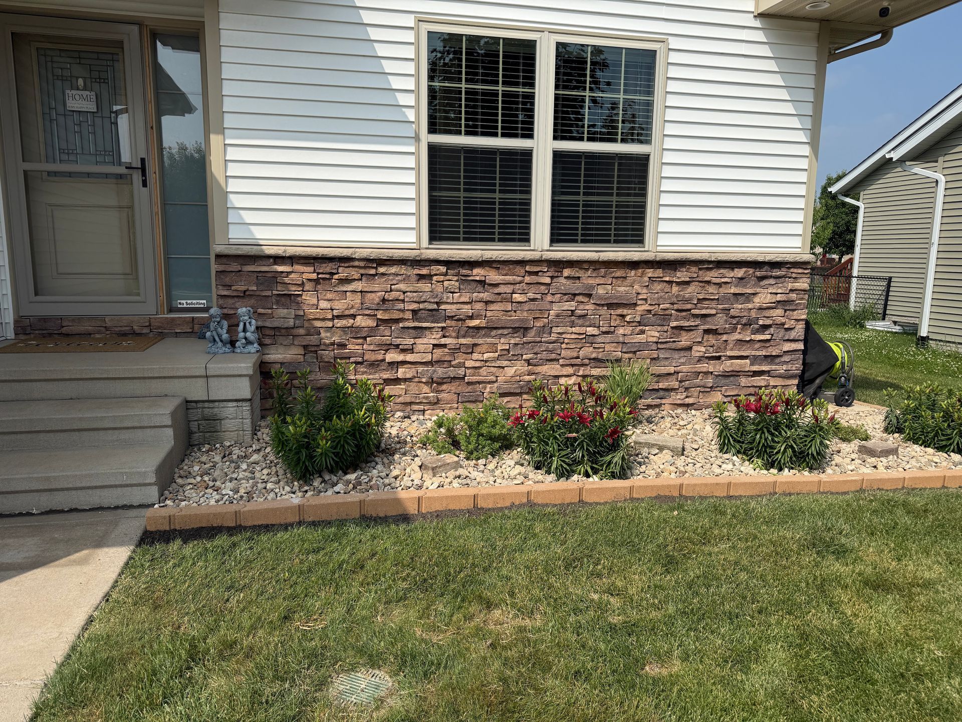 House front with stone and siding facade, front porch, windows, and landscaped flower bed along the lawn.