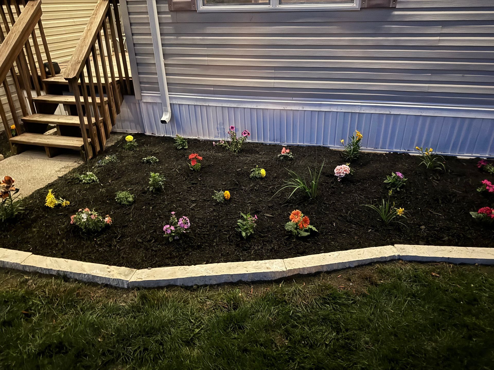 Front yard flower bed with small colorful blooms along a house and wooden steps