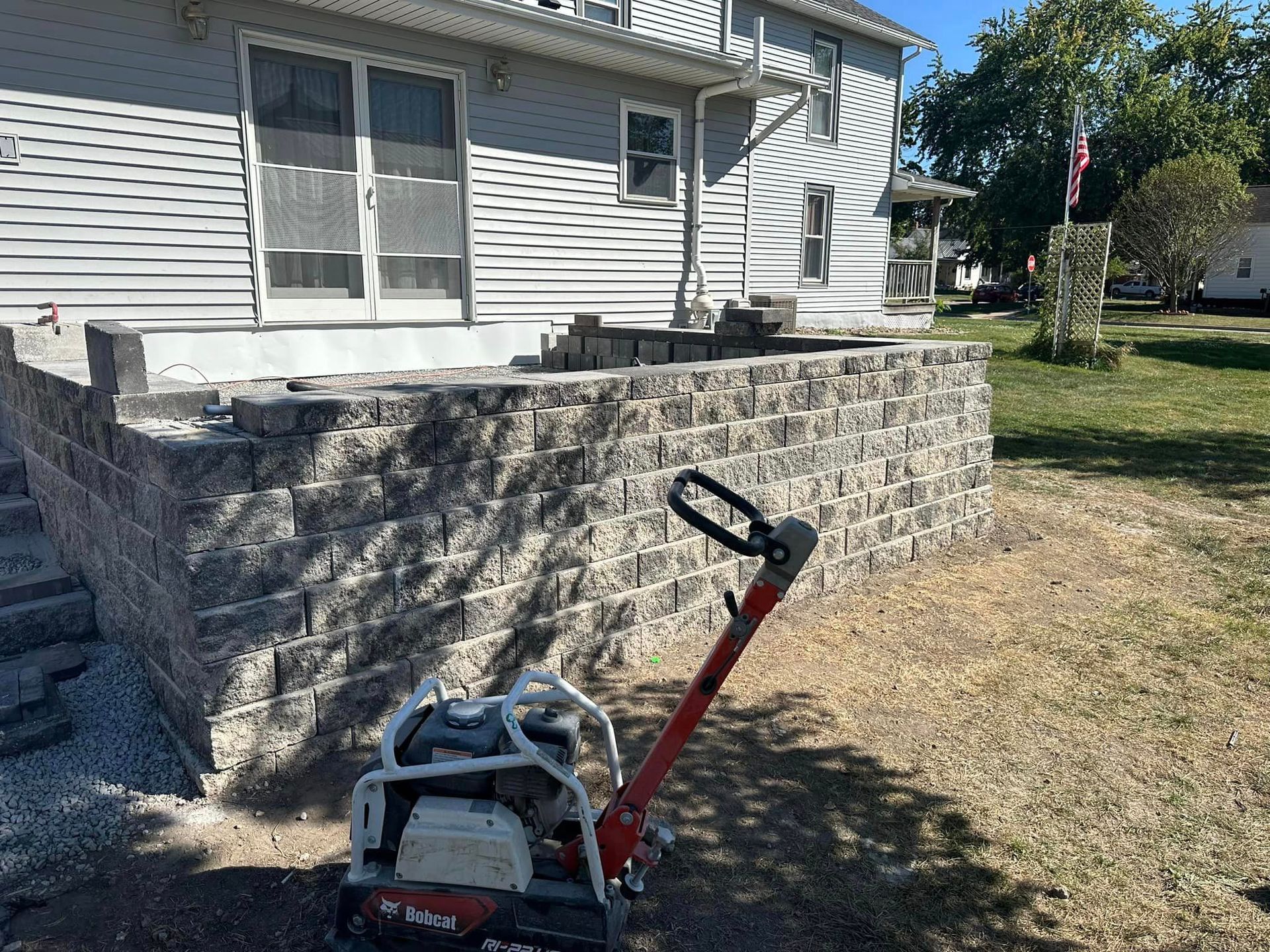 Red push lawn mower in front of a stone retaining wall beside a house and yard