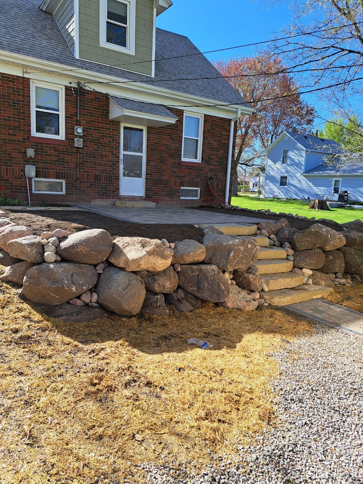 Stone retaining wall and steps beside a brick house with a snowy yard on a sunny day