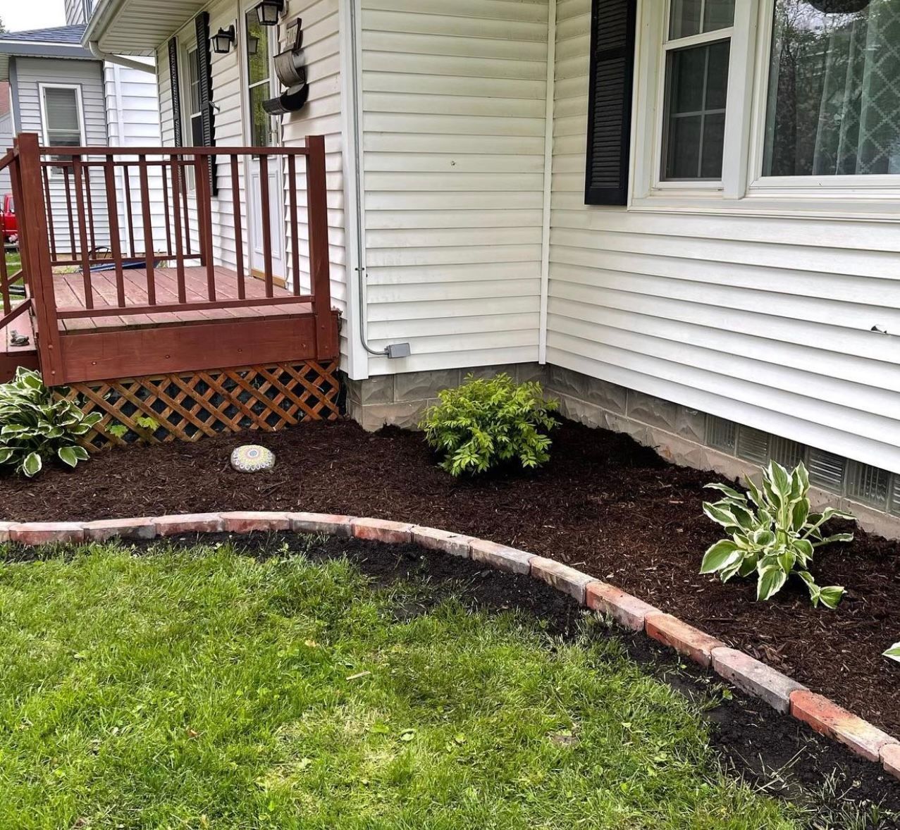 Curved garden bed with mulch and plants beside a house porch and lawn