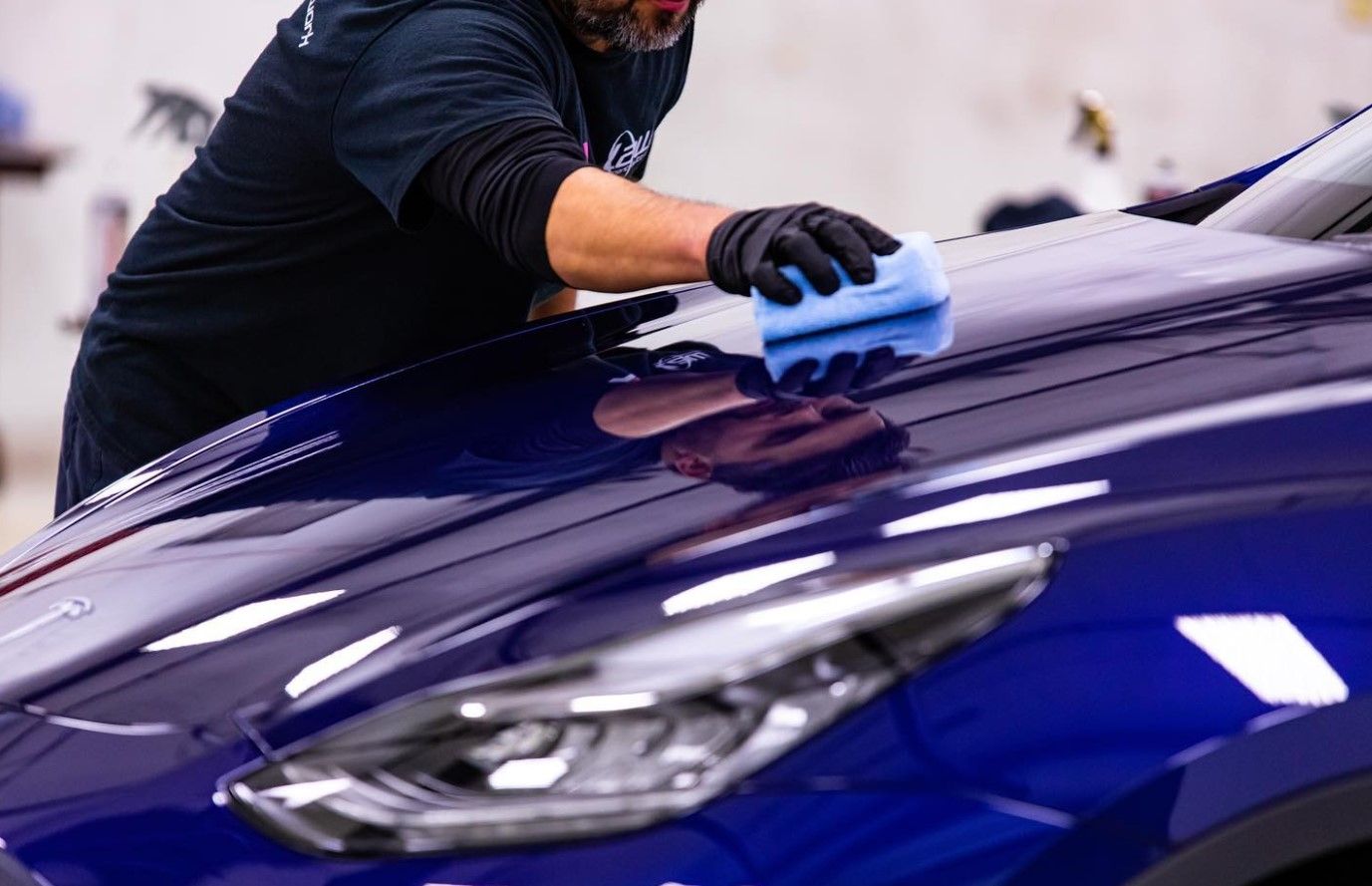 Person applying ceramic coating to a shiny blue car hood with a sponge in a garage.
