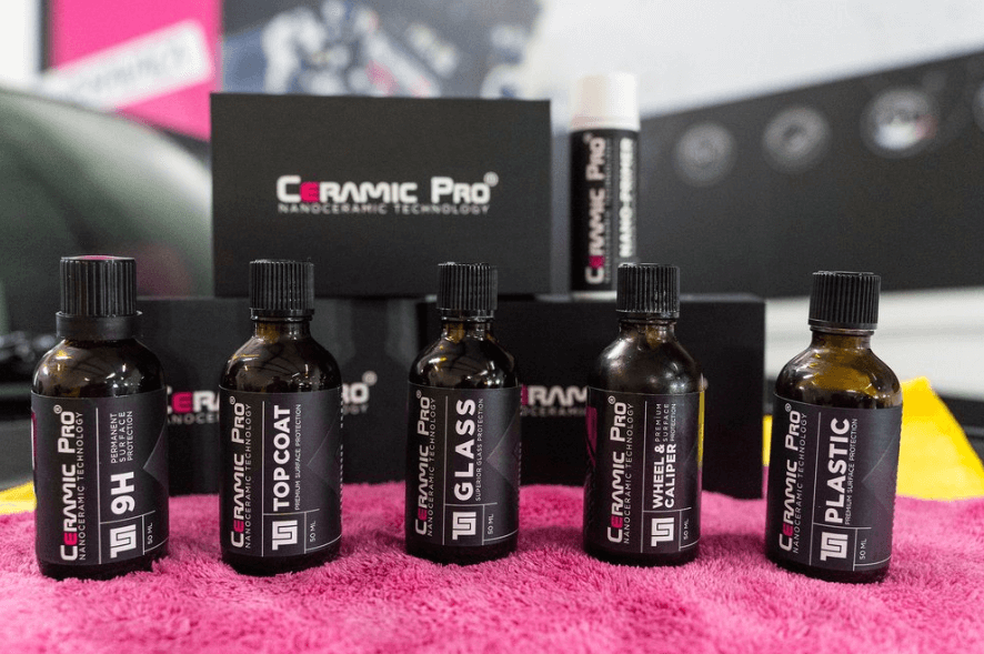 Ceramic Pro car detailing products: 9H, Top Coat, Glass, Light, and Plastic bottles on pink cloth.