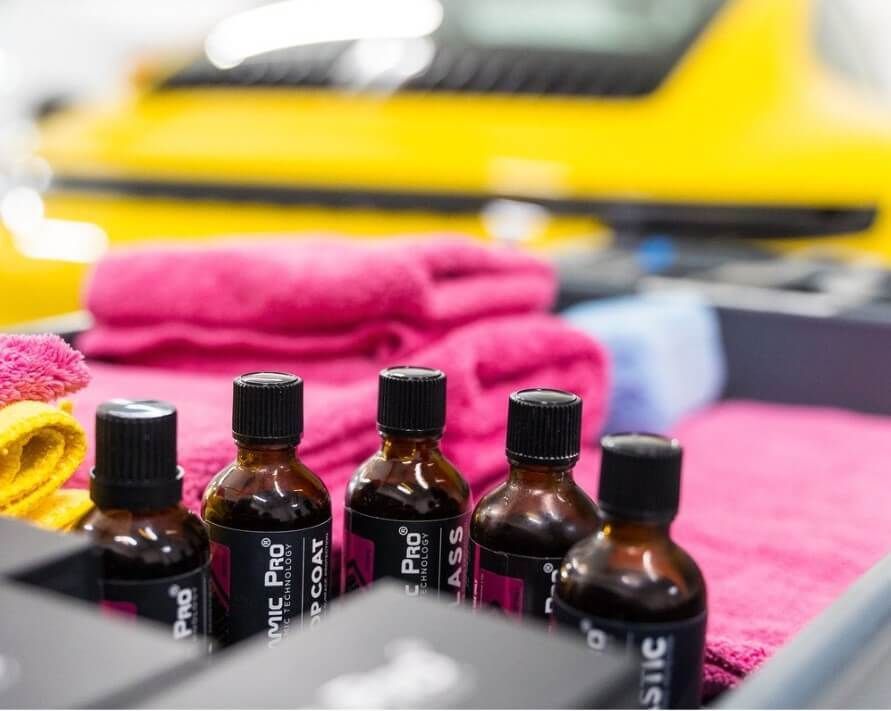 Bottles of car detailing products with towels, yellow car in the background.