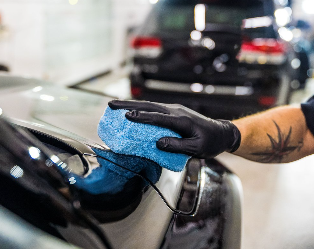 Person in black gloves polishing a black car with a blue cloth.