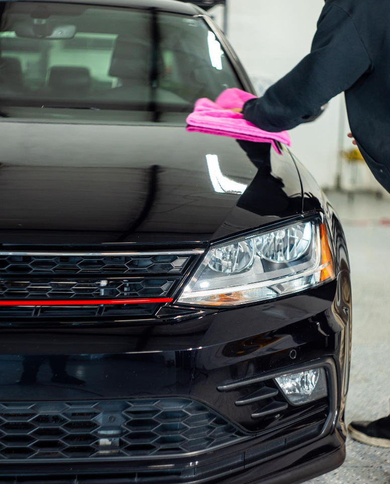 Person polishing a shiny black car with a pink cloth.